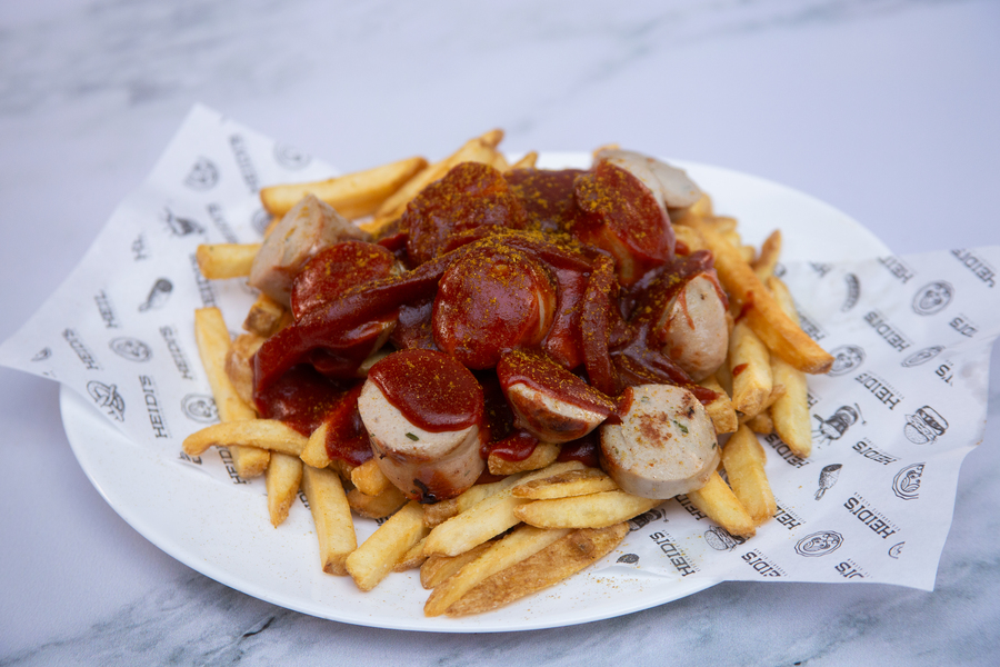 Especialidades de Salchichas preparadas en Heidi's CURRYWURST POMMES Salchicha asada a la parrilla cortada en rebanadas sobre una cama de papas a la francesa con su salsa a base de tomate, cátsup, cebolla, curry y otros ingredientes de la receta original de platillo inventado en 1949 por la Sra. Herta Heuwer en Berlín.